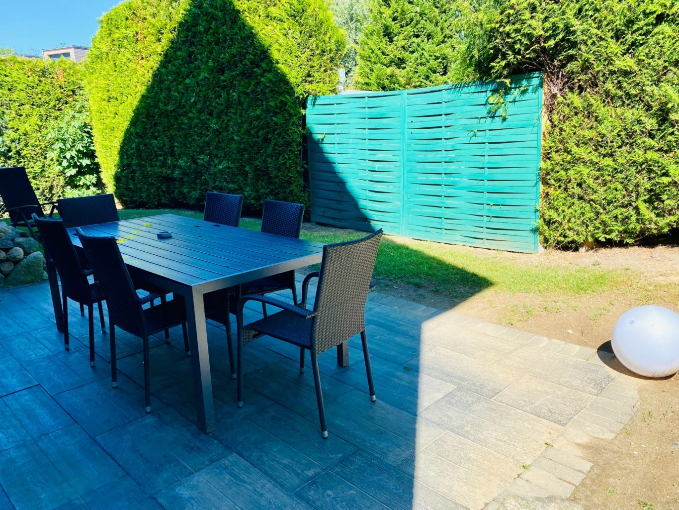Sonniger Garten & Terrasse in der Ferienwohnung Meeresbrise Gartenbereich mit Tisch, Stühlen, Hecke und einer schönen abendlichen Beleuchtung in der Ferienwohnung Meeresbrise