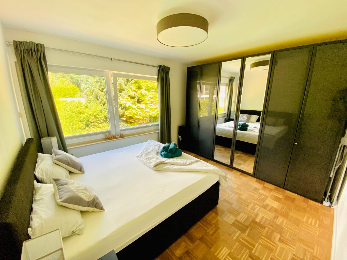 Helles Schlafzimmer mit viel Stauraum & Gartenblick Helles Schlafzimmer mit Doppelbett, großen Fenstern und einem Schrank mit Spiegeltüren.