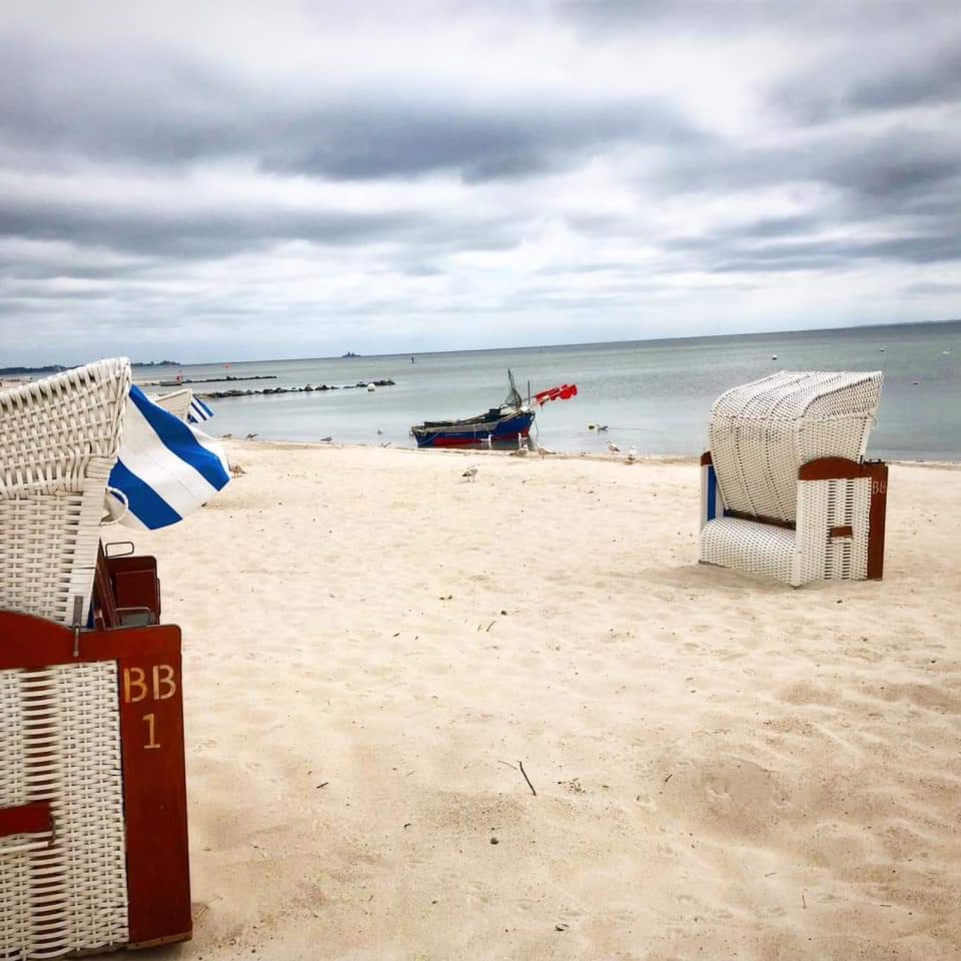Nur 250 m zum Strand Strand mit zwei Strandkörben, Boot im Hintergrund und bewölkter Himmel.